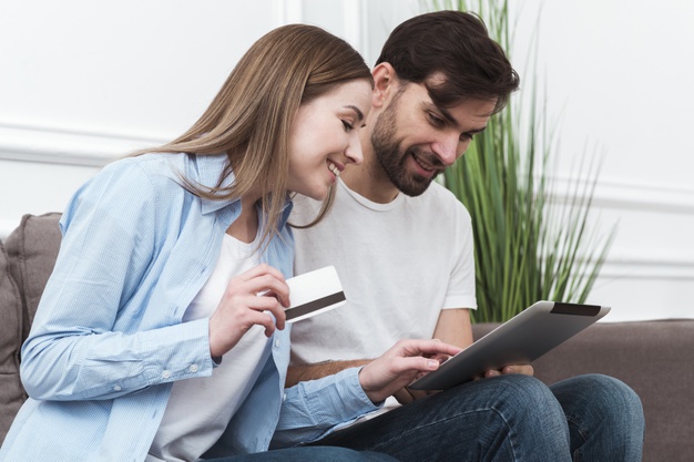 Como identificar um bom pagador. Um casal fazendo compras online por meio de um tablet e sorrindo.