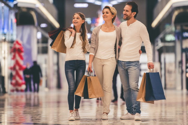 Tendências novo consumidor em 2020. Três pessoas da família andando no shopping com sacolas nas mãos e olhando as vitrines das lojas.
