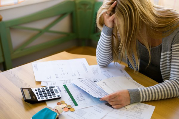 Inadimplência. Mulher apoiando a testa na mão com contas e calculadoras em cima da mesa.